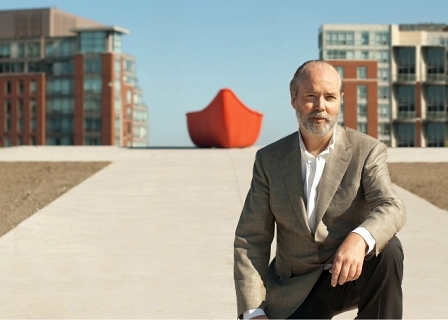 Douglas Coupland in einem beigen Jackett kniet vor einem roten Schiff